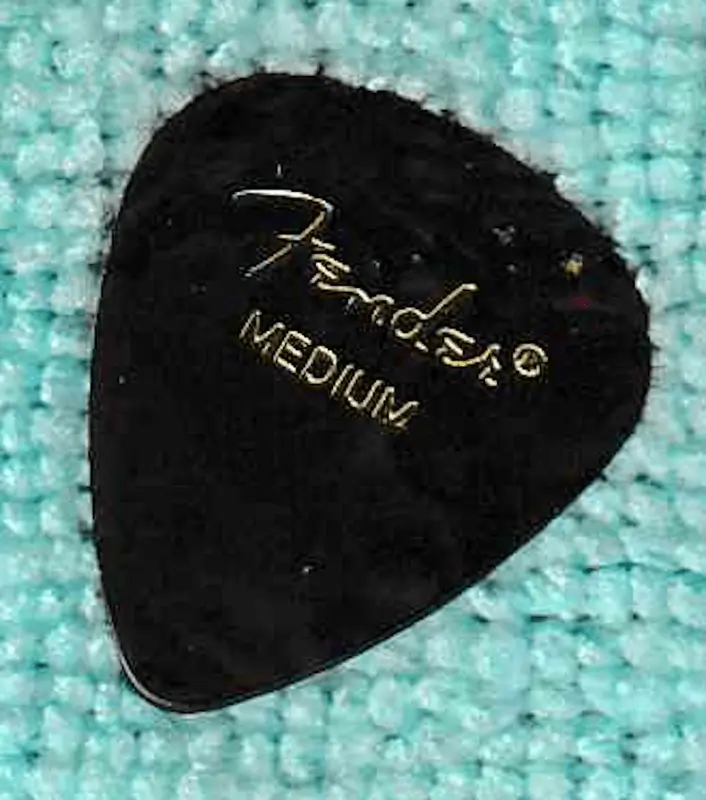 An Example of a #451 Pick By Fender in Medium Gauge with dark Celluloid Composition. Against a blue background.