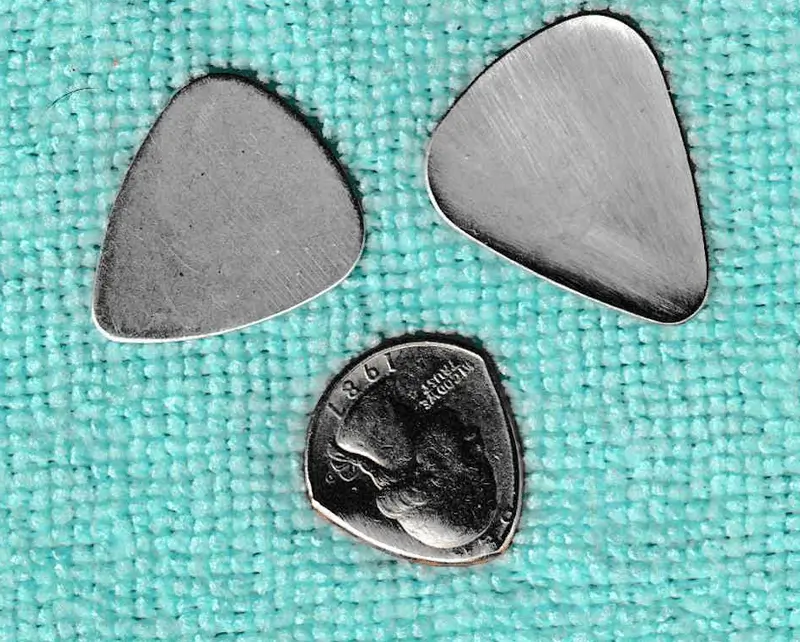 3 of my metal picks, a quarter of Cupronickle on the bottom, Aluminum on the top left and Stamped Steel on the top right, On top of blue cloth.