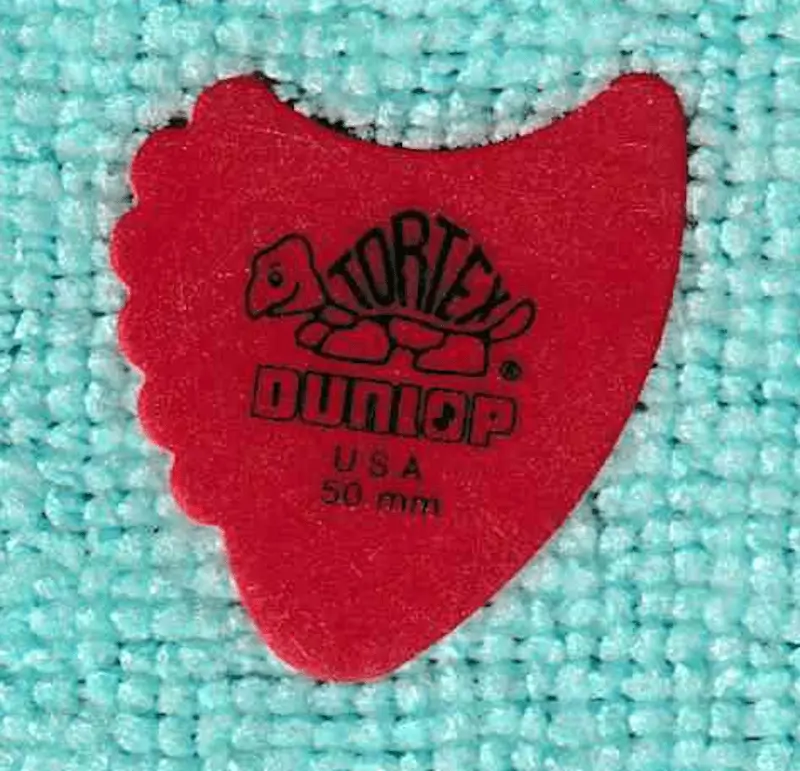 The modern classic "Sharkfin" style plectrum by Dunlop. 50mm in red, note scallops on left side and hook end on right, with blunt end on bottom.