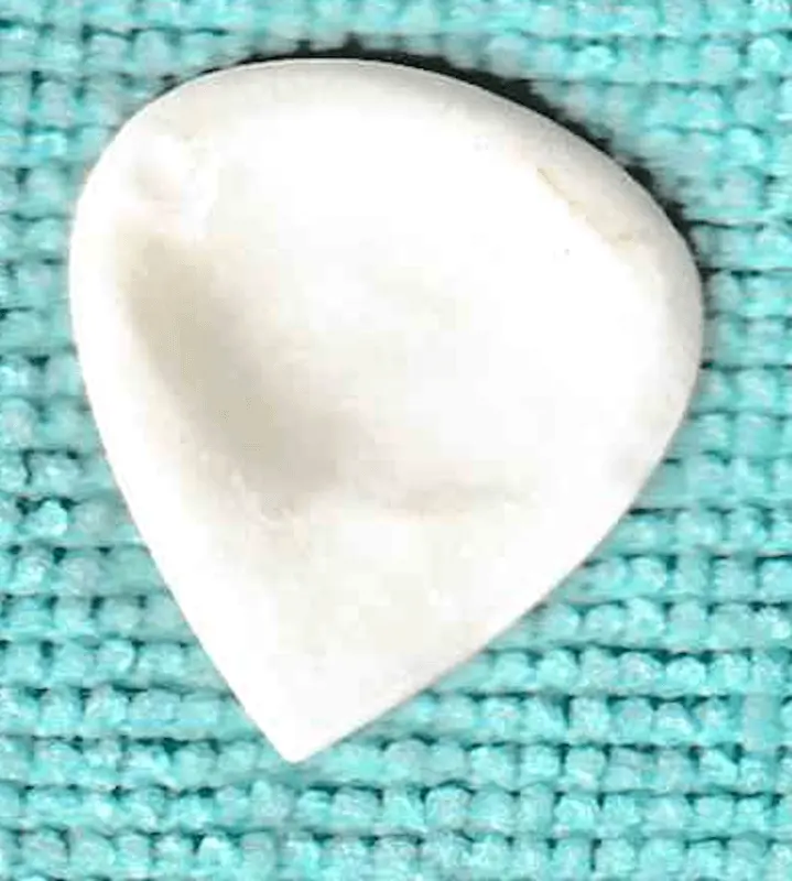 The GuitarHeads Camel Bone Plectrum in White of Broad angled teardrop shape with fine tip against blue cloth for contrast.