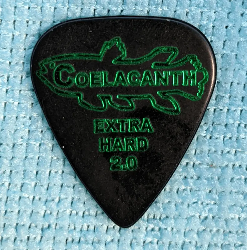 The Spin-Top Shaped Ebonya Ebonite Extra Hard 2.0 Pick. Coelacanth Trade Mark set against Blue Cloth for display. Note the aggressive shape.