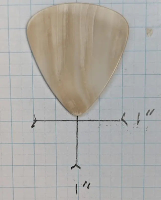A beautifully striated Natural sea shell pick by Beachside Picks against 1/4" ruled Graph Paper for Sizing.