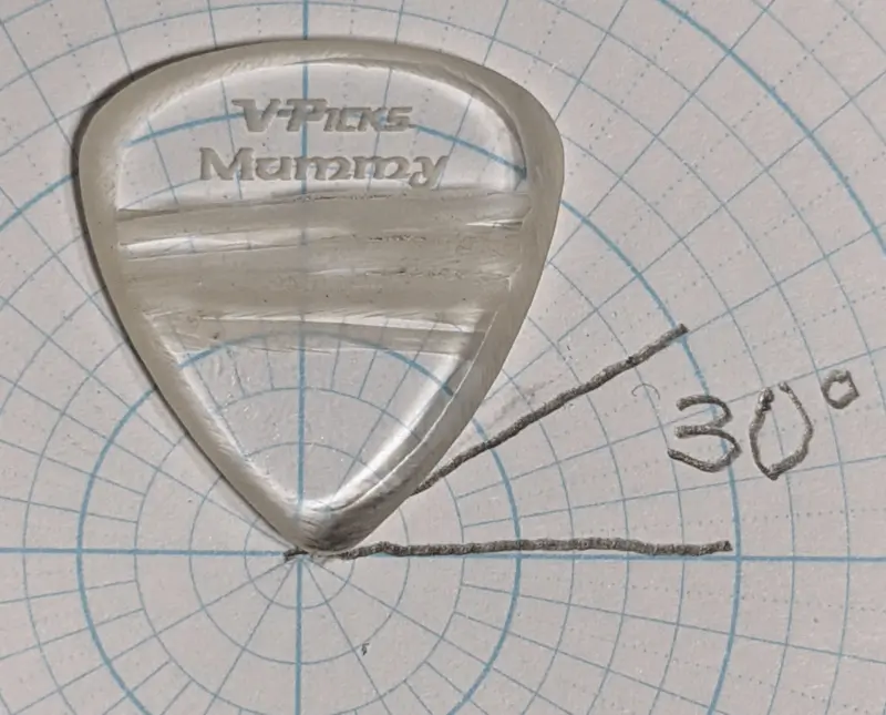 The thick Acrylic V-Picks Mummy brand rough edged clear pick against circular/angle ruled paper for shape reference.