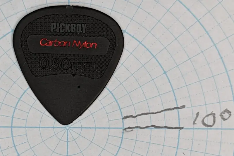 Pickboy's carbon nylon pick on top of circular ruled angle paper for shape reference.