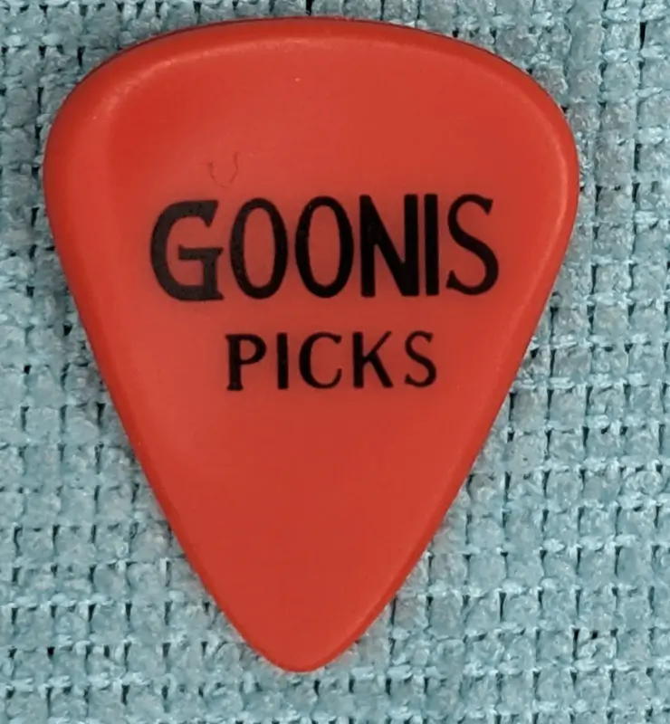 Introducing an innovative design, a red Goonis Brand grip relieves pick against blue background, note asymmetric shaping.
