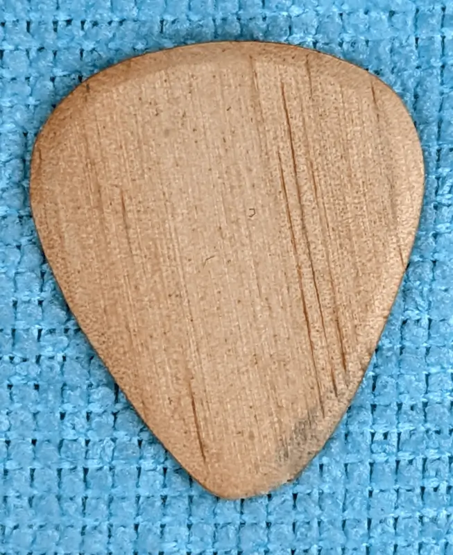 The IskraWoodcrafts Pine pick, that was given as a bonus Pick on an order. Shown against blue cloth background. Note nickle metal discoloration from use.