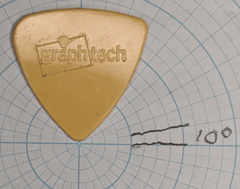 Reverse View of the Medium sounding material Graphtech tri-tip guitar pick on circular/angle ruled graph paper for shape reference.