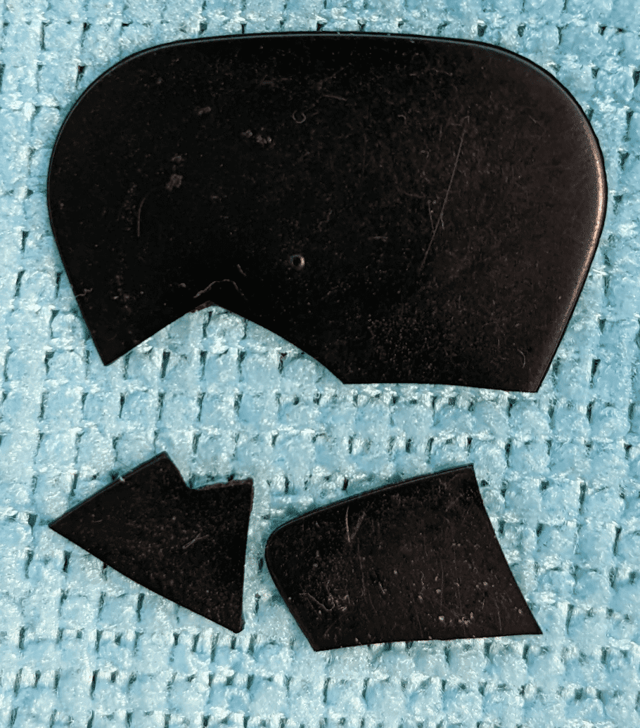 A broken Ebonite Pick set on top of Blue cloth no longer playable. Light Gauge. Remaining pieces, note hardness tool indent.