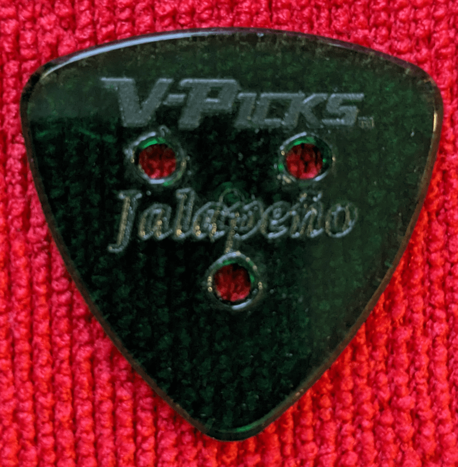 An obverse view of the V-Picks Jalapeno 3 holed green pick against a bright red backdrop.