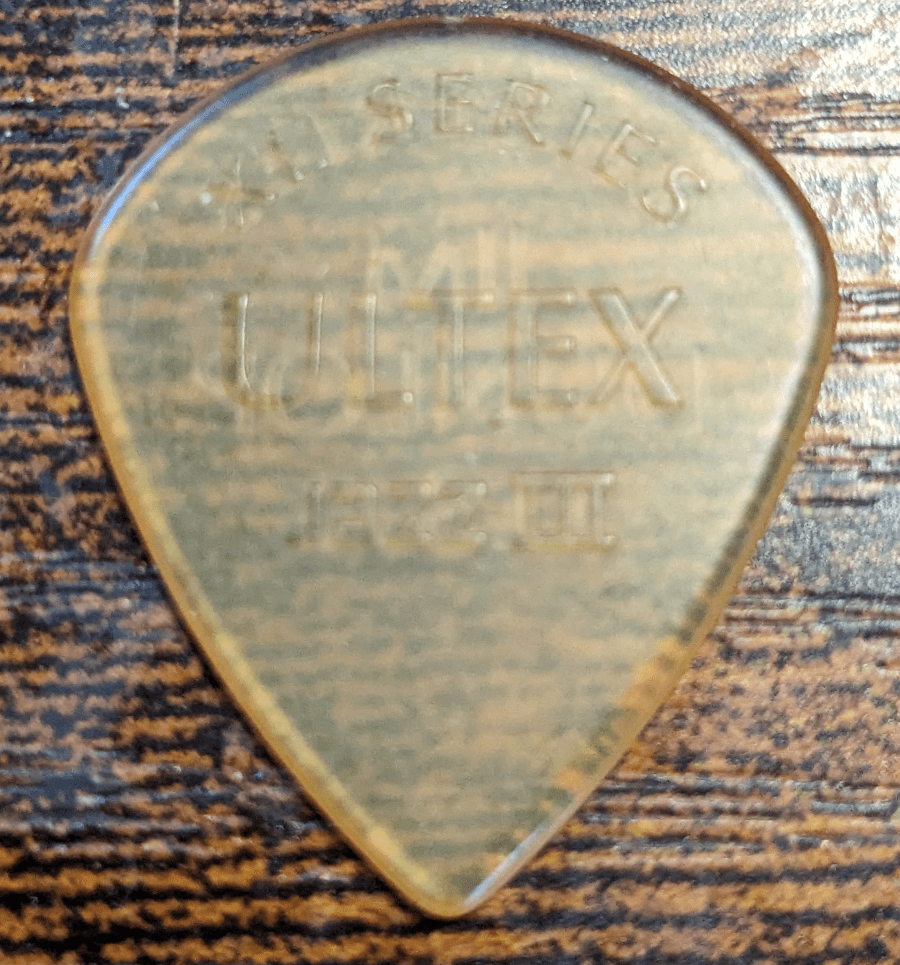 The Jim Dunlop XL Series Brand Ultex Plastic Jazz III shaped pick on top of wood grain for your viewing pleasure.