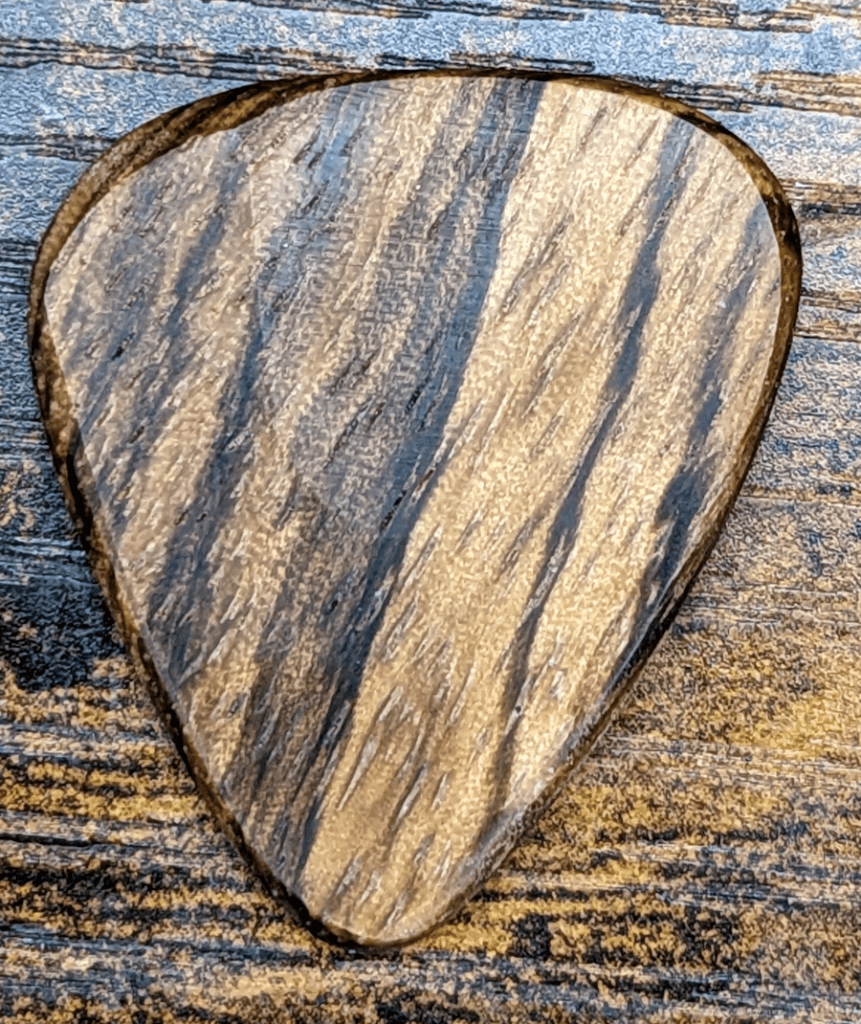 The Pickslay Brand Zebra Wood Guitar Pick on Wooden background Revealing its beauty