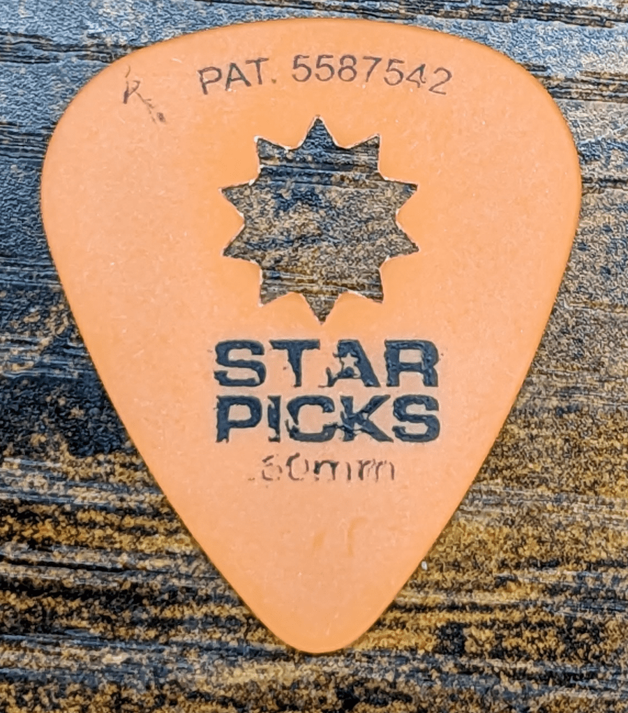 The Everly Brand Orange Star Pick Against Wood backdrop