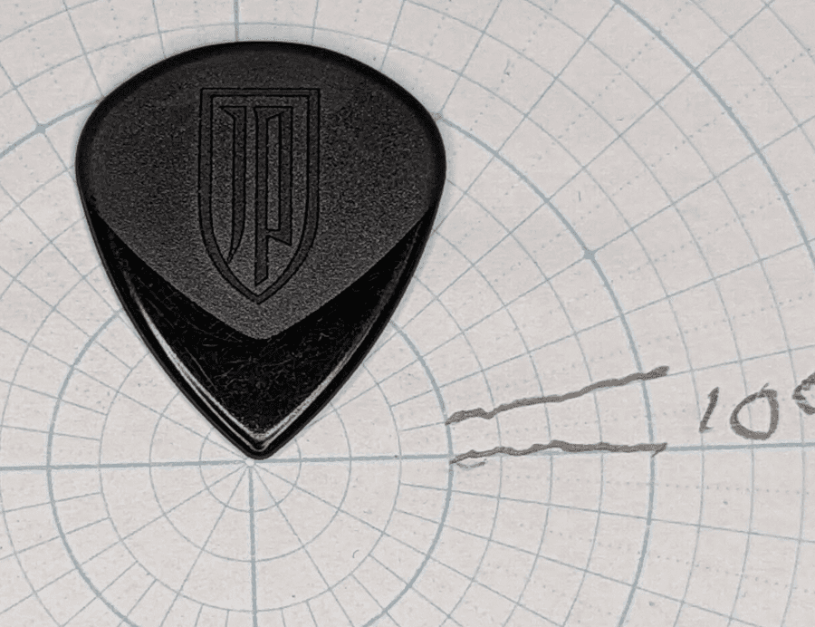 The Black Dunlop JP Embossed Pick with a background of cicular Angle Paper for reference