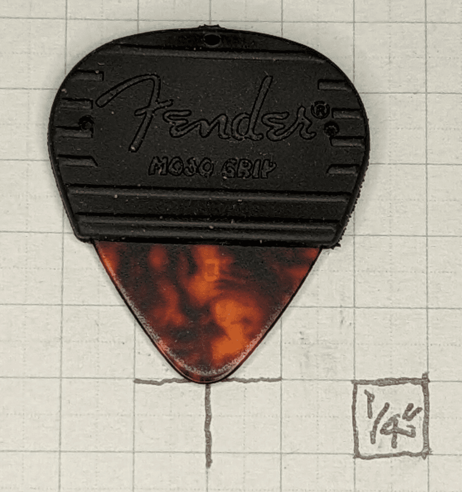 Our Fender Medium Mojo Grip Covered Celluloid Pick is pictured against 1/4" ruled graph paper for sizing reference.