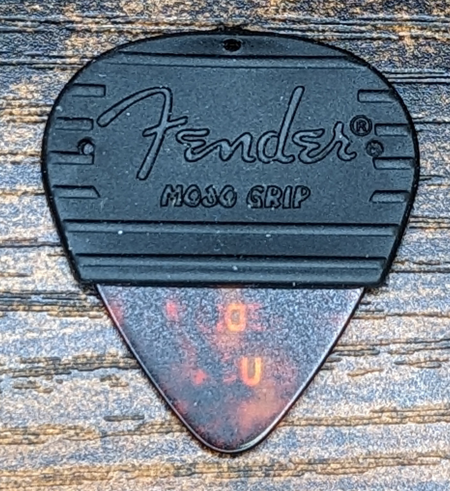 Image of the famous Fender Medium Mojo Grip covered pick against a wood surface.