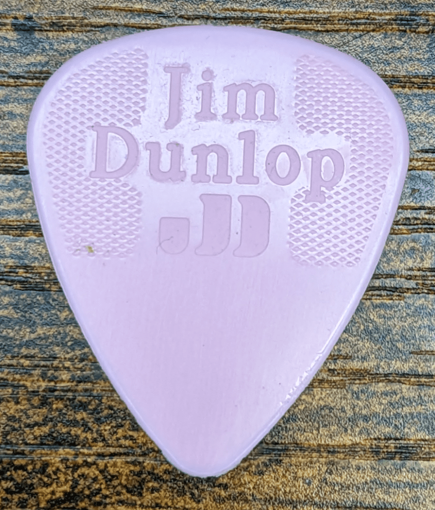 The Fat Mike Signature Jim Dunlop Brand Pink Guitar Pick Reverse Side against Wood Grain