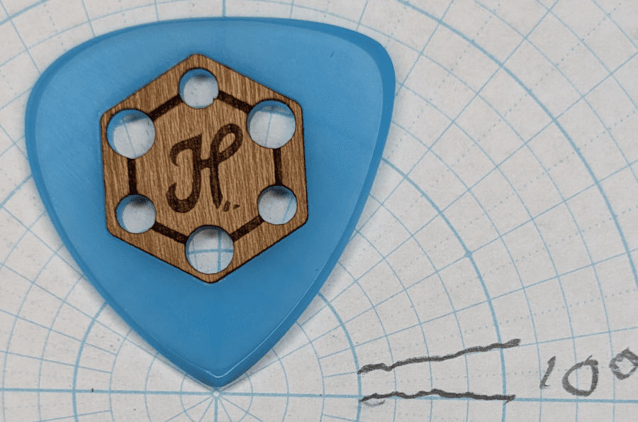 The Blue Glow Cast Wooden Grip Honey Pick Guitar Pick. A Glow Worm Three Tipped Super Guitar Pick of Acrylic Against Angle Paper.